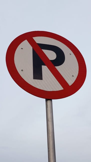 A UK 'no parking' sign featuring a circular design with a red border and a diagonal red slash across a black letter 'P' on a white background, mounted on a metallic pole against an overcast sky. This sign indicates parking restrictions commonly seen in areas where house removals or furniture transport are carried out, such as during home relocation or moving services managed by Removal Companies Harringay, ensuring compliance with local parking rules on busy streets or residential neighbourhoods.